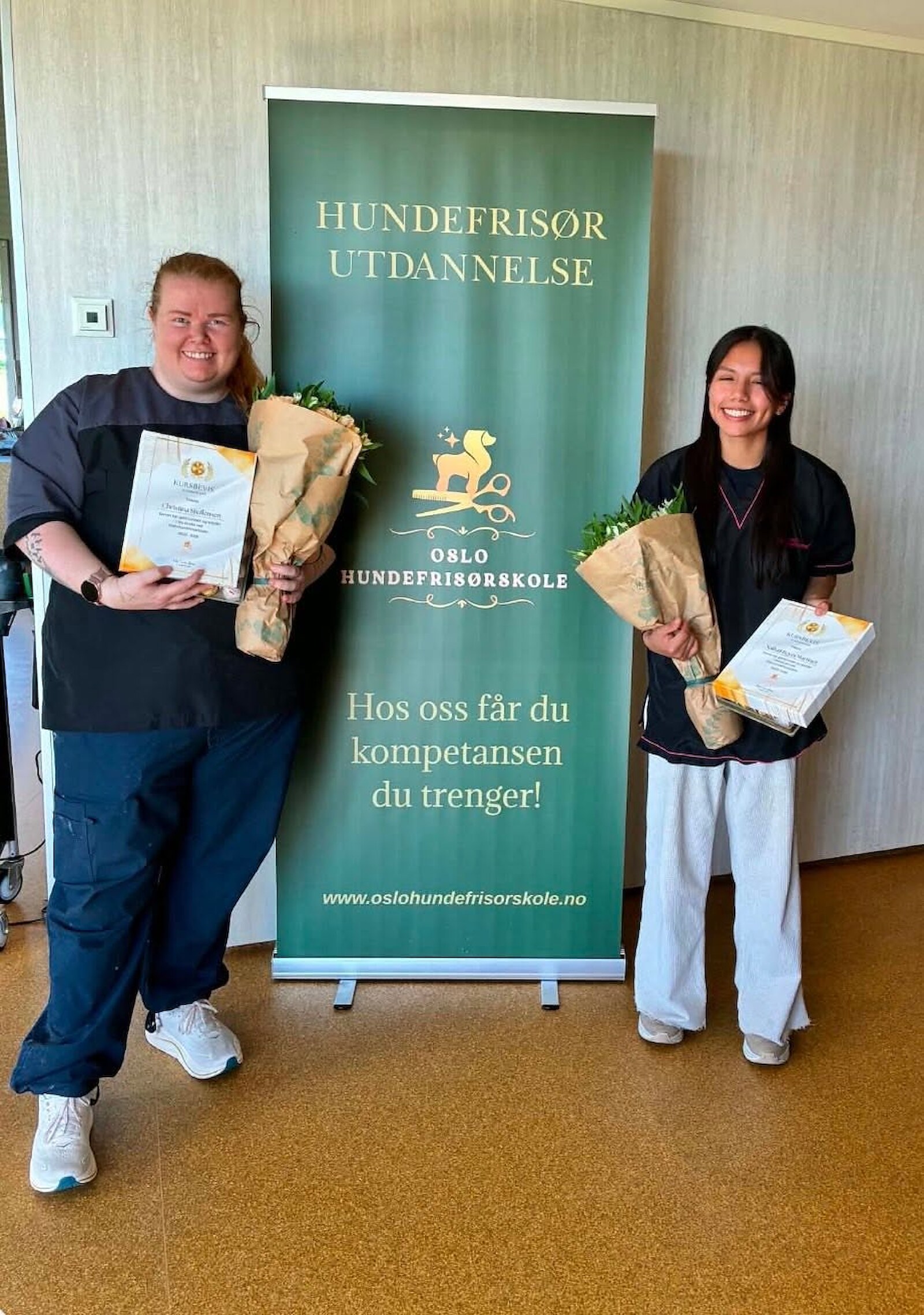 To studenter med diplom og blomster foran roll-up-banneret til Oslo Hundefrisørskole